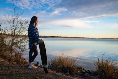 Image of a brunette girl looking out into the distance with her skateboardの写真素材