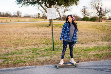 Image of brunette girl skateboarding wearing pink earmuffs and smiling at the cameraの写真素材