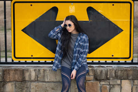 Candid image of a beautiful brunette girl sitting on a brick wall against a road signの写真素材
