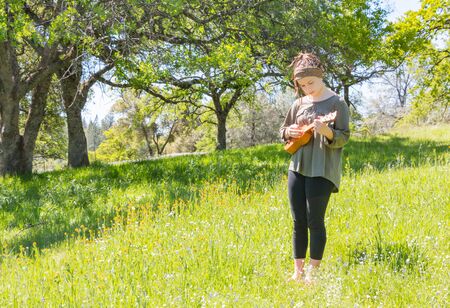 Cute Young Girl With Ukulele in Green Grassy Fieldの写真素材