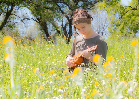 Cute Young Girl With Ukulele in Green Grassy Fieldの写真素材