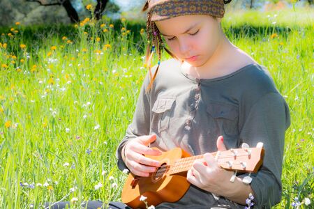 Cute Young Girl With Ukulele in Green Grassy Fieldの写真素材