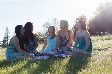 Group of Girls Sitting Together in Grassy Field With Sunlight Overheadの写真素材