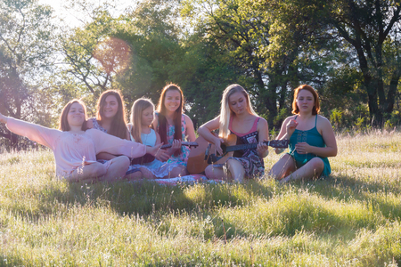 Young Girls Sitting Together in Grassy Field Singing and Playing Musical Instruments With Sunlight Overheadの写真素材