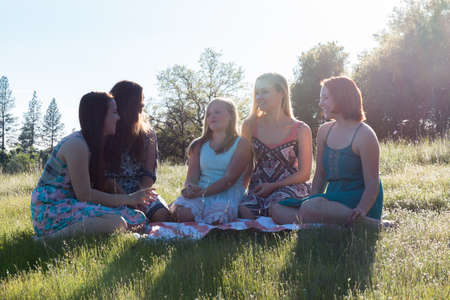 Group of Girls Sitting Together in Grassy Field With Sunlight Overheadの写真素材