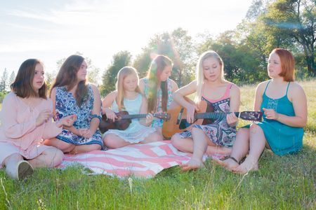 Young Girls Sitting Together in Grassy Field Singing and Playing Musical Instruments With Sunlight Overheadの写真素材