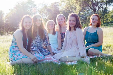 Group of Girls Sitting Together in Grassy Field With Sunlight Overheadの写真素材