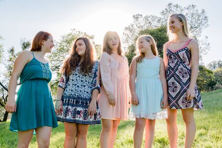 Young Girls Standing Together in Green Field With Trees in the Background and Sunlight Overheadの写真素材