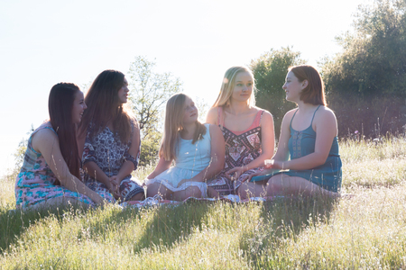 Group of Girls Sitting Together in Grassy Field With Sunlight Overheadの写真素材