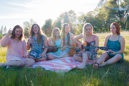 Young Girls Sitting Together in Grassy Field Singing and Playing Musical Instruments With Sunlight Overheadの写真素材
