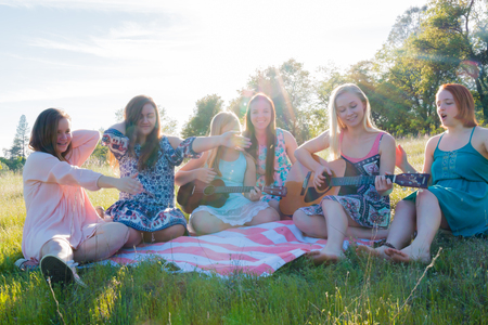 Young Girls Sitting Together in Grassy Field Singing and Playing Musical Instruments With Sunlight Overheadの写真素材