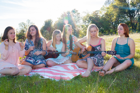 Young Girls Sitting Together in Grassy Field Singing and Playing Musical Instruments With Sunlight Overheadの写真素材