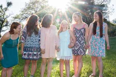 Young Girls Standing Together in Green Field With Trees in the Background and Sunlight Overheadの写真素材