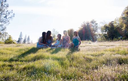 Group of Girls Sitting Together in Grassy Field With Sunlight Overheadの写真素材
