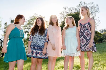 Young Girls Standing Together in Green Field With Trees in the Background and Sunlight Overheadの写真素材