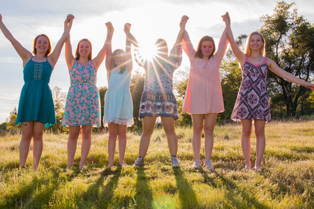 Group of Girls Standing With Arms Raised and Sunlight Overheadの写真素材
