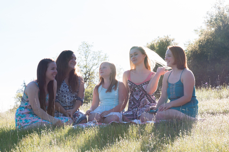 Group of Girls Sitting Together in Grassy Field With Sunlight Overheadの写真素材