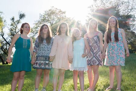 Young Girls Standing Together in Green Field With Trees in the Background and Sunlight Overheadの写真素材