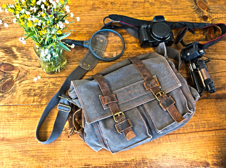 Bleu Satchel With Camera, Tripod and Magnefying Glass Sitting on Wooden Tableの写真素材