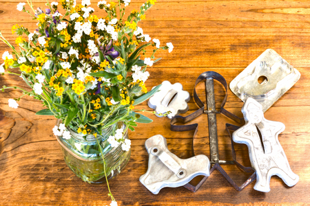 Tin Cookie Cutters and Flowers in Glass Vase Sitting on Wooden Table With Knotsの写真素材