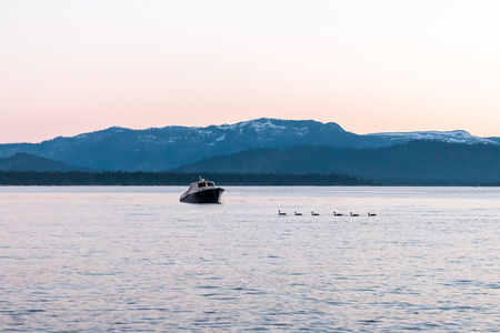 View of Ducks and Small Boat on a Blue Lake With Mountians in Backgroundの写真素材