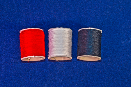 Three Color Cotton Reel Spools of Sewing Thread on Blue Background