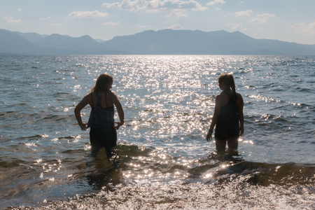Silhouette of Two Young Girls With Raised Arms in the Water at the Beachの写真素材