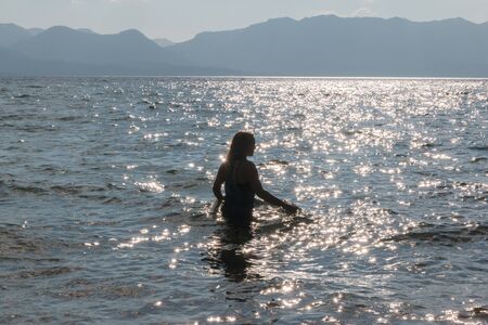 Silhouette of One Young Girl With Raised Arms in the Water at the Beachの写真素材