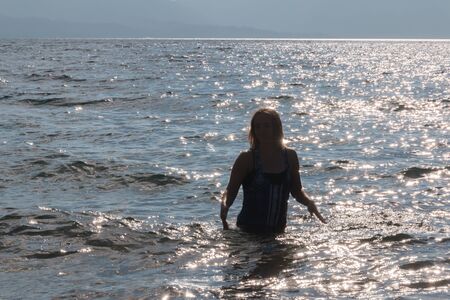 Silhouette of One Young Girl With Raised Arms in the Water at the Beachの写真素材