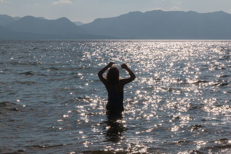 Silhouette of One Young Girl With Raised Arms in the Water at the Beachの写真素材