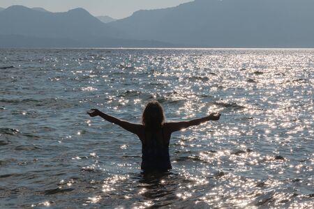 Silhouette of One Young Girl With Raised Arms in the Water at the Beachの写真素材