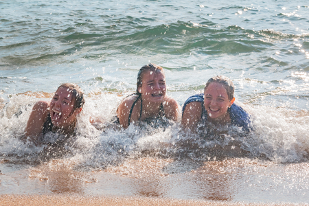 Beautiful Young Girls Lay on the Sand While Waves Splash Over Them at the Beachの写真素材