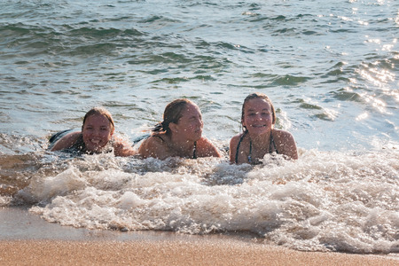 Beautiful Young Girls Lay on the Sand While Waves Splash Over Them at the Beachの写真素材