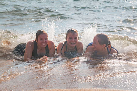 Beautiful Young Girls Lay on the Sand While Waves Splash Over Them at the Beachの写真素材