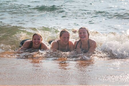 Beautiful Young Girls Lay on the Sand While Waves Splash Over Them at the Beachの写真素材