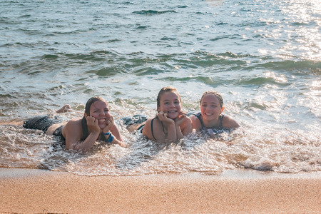 Beautiful Young Girls Lay on the Sand While Waves Splash Over Them at the Beachの写真素材