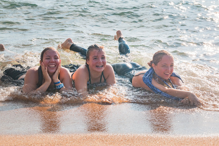 Beautiful Young Girls Lay on the Sand While Waves Splash Over Them at the Beachの写真素材