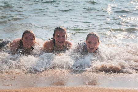 Beautiful Young Girls Lay on the Sand While Waves Splash Over Them at the Beachの写真素材