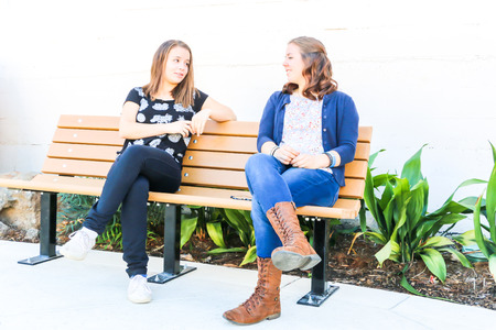 Two Young Girls Sitting on City Bench Togetherの写真素材