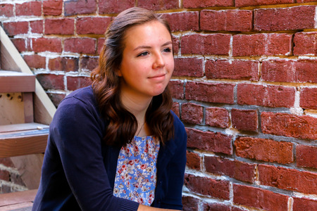 Young Girl Sitting on Stairway Next to an Old Red Brick Wallの写真素材