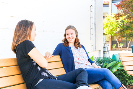 Two Young Girls Sitting on City Bench Togetherの写真素材