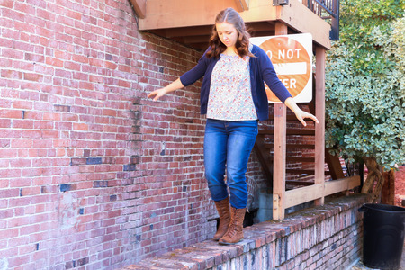 Young Girl Playing and Balancing on Old Red Brick Wallの写真素材