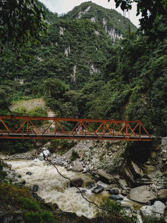 orange-colored bridge over a mighty river and in the background an incredible mountain range.の写真素材