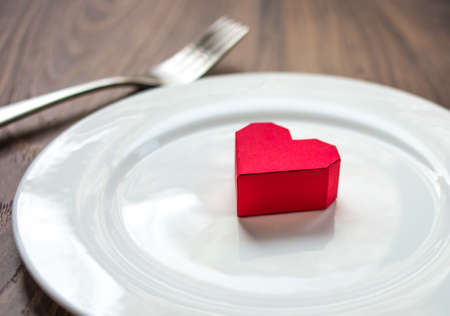 Red heart on a plate, fork and knife on wooden background