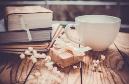 Books, flowers, white cup and wrapped gift box on wooden tableの写真素材