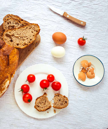 Bread, boiled eggs and cherry tomatoes on white tableの写真素材