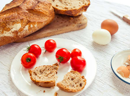 Bread, boiled eggs and cherry tomatoes on white tableの写真素材