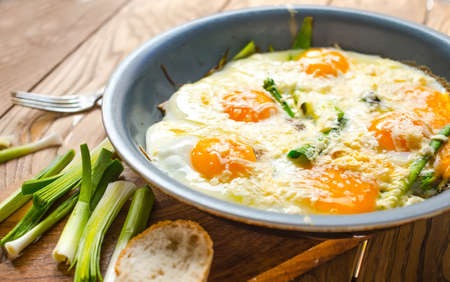 Scrambled eggs with leek in pan on wooden tableの写真素材