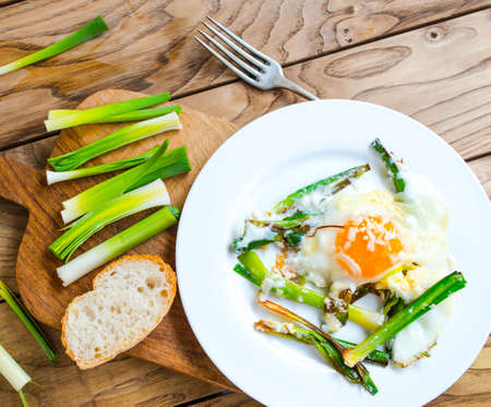 Scrambled eggs with leek on white plate on wooden tableの写真素材