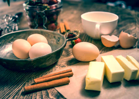 Eggs, butter, cinnamon, strawberry - ingredients for pastry on wooden table.の写真素材